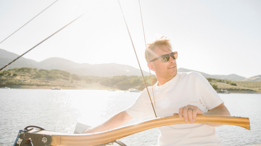 Hombre con gafas de sol navegando en un velero durante el atardecer